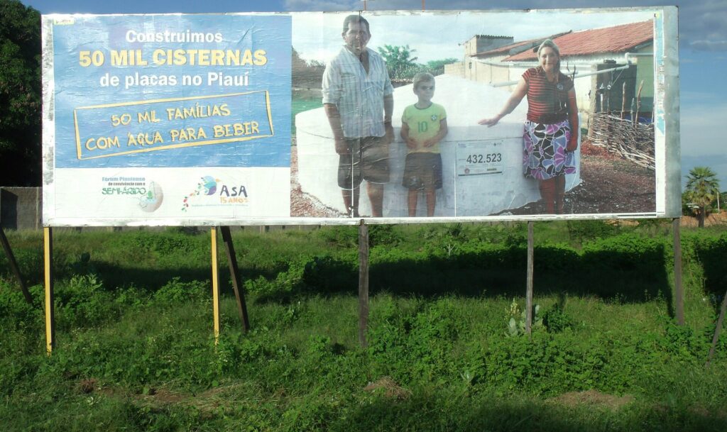 Placa do programa de cisternas da ASA no Piauí anunciando 50 mil cisternas de placas, com família em frente a uma cisterna