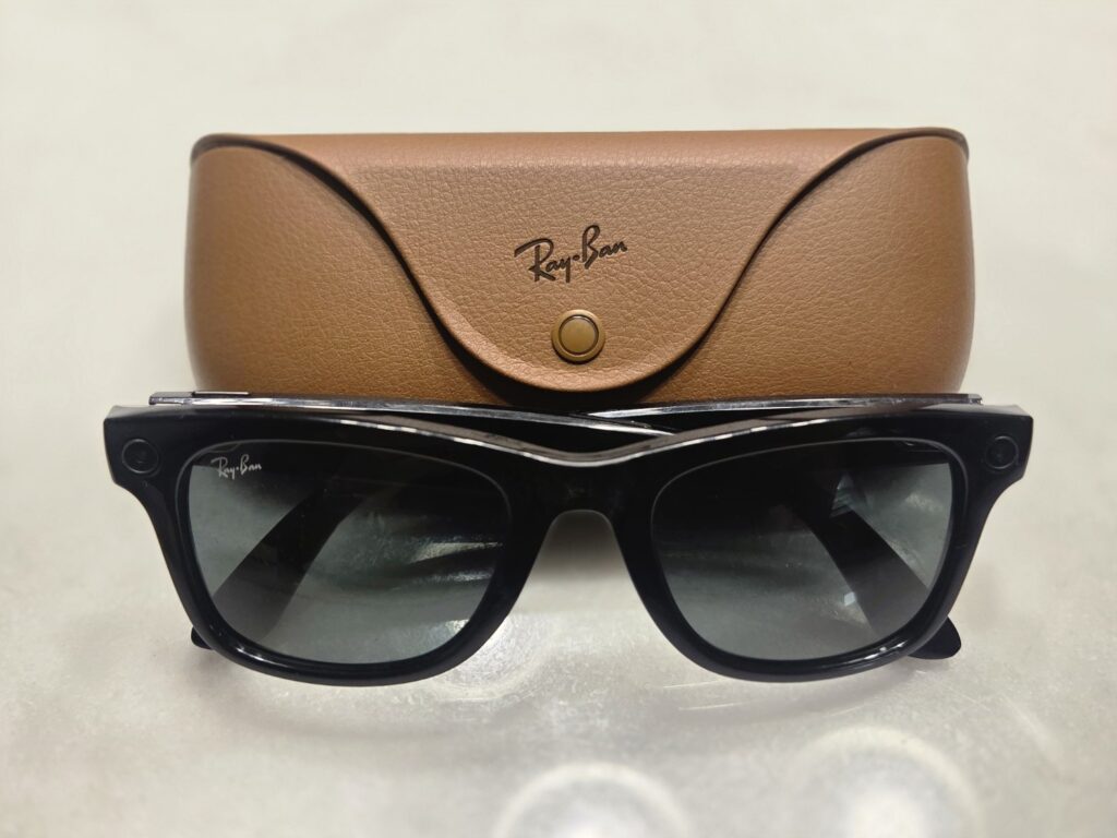 Óculos inteligentes Ray-Ban Meta pretos, com câmera na armação, diante do estojo de couro marrom
