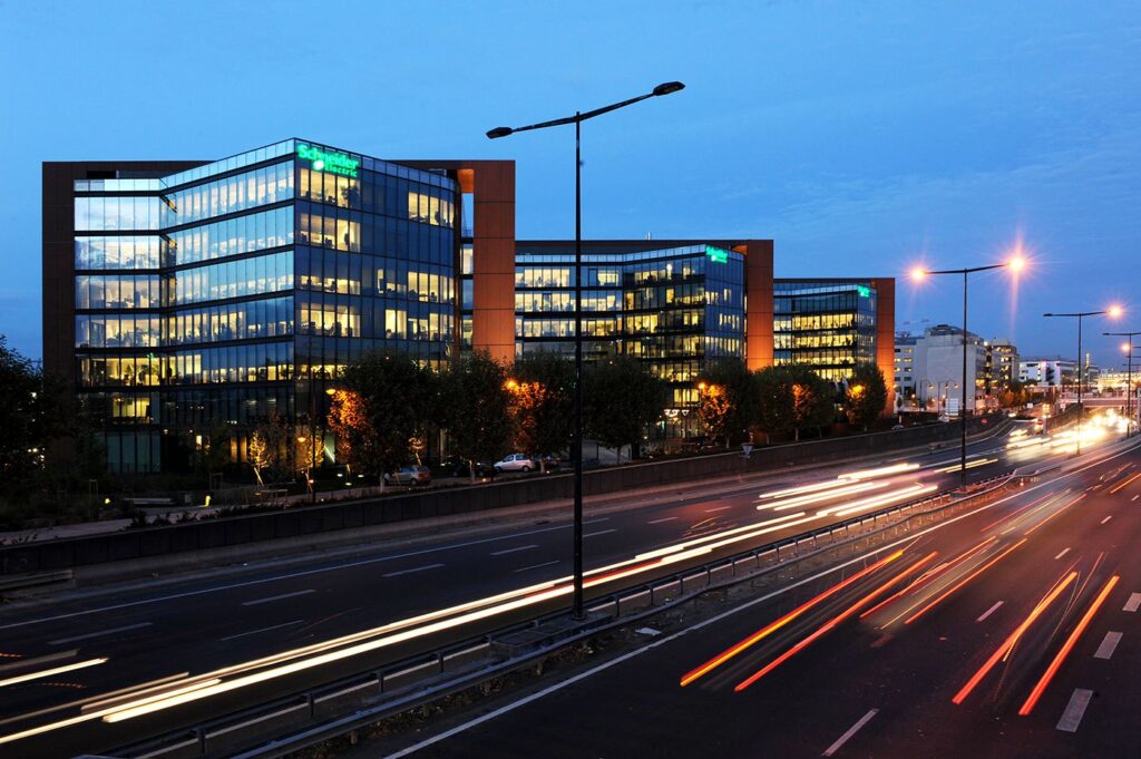 Sede da Schneider Electric em Rueil-Malmaison, França, iluminada ao entardecer com rastros de luz de carros