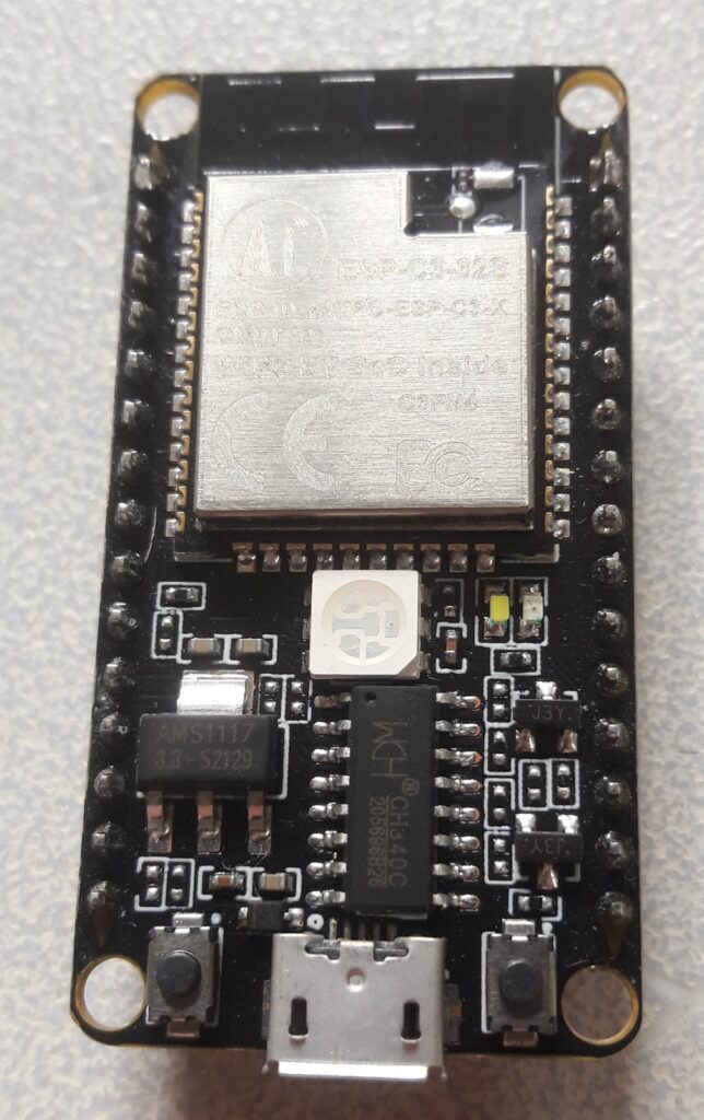 Placa de desenvolvimento preta com o módulo ESP32-C3 prateado, pinos laterais, dois botões e conector micro-USB